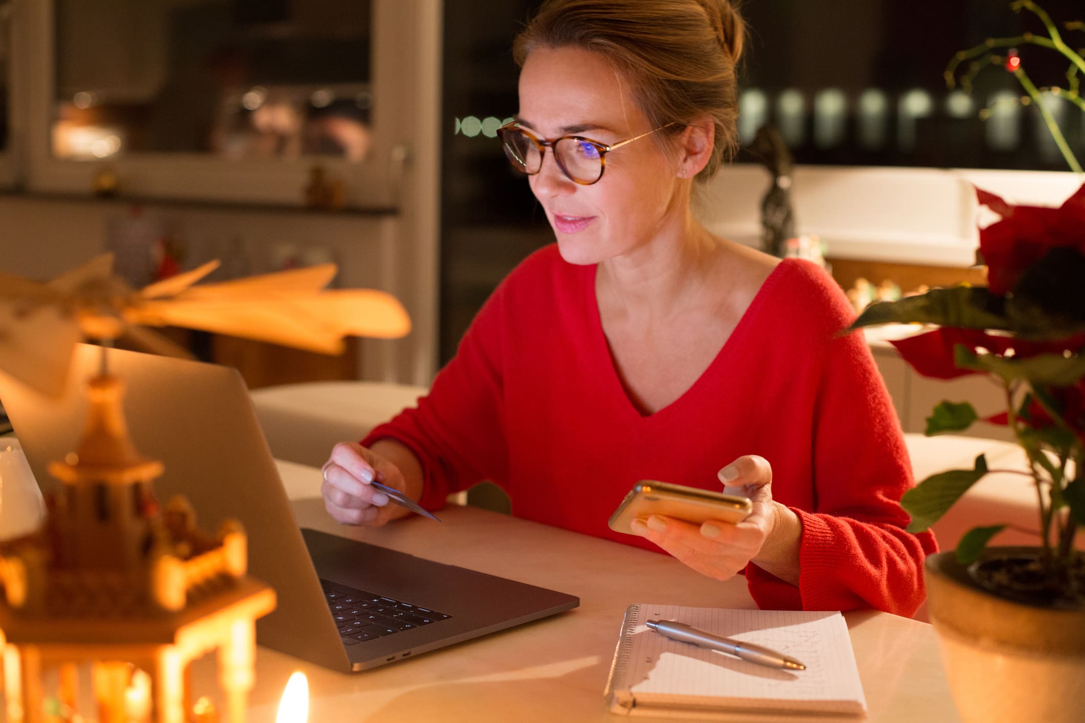 Egy szemüveges nő a számítógép előtt online vásárol, bankkártyával a kezében.