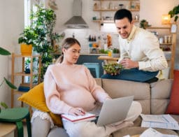 Egy várandós nő néz valamit a számítógépen, kezében papírok. A férje is rápillant a monitorra, megbeszélnek valamit.