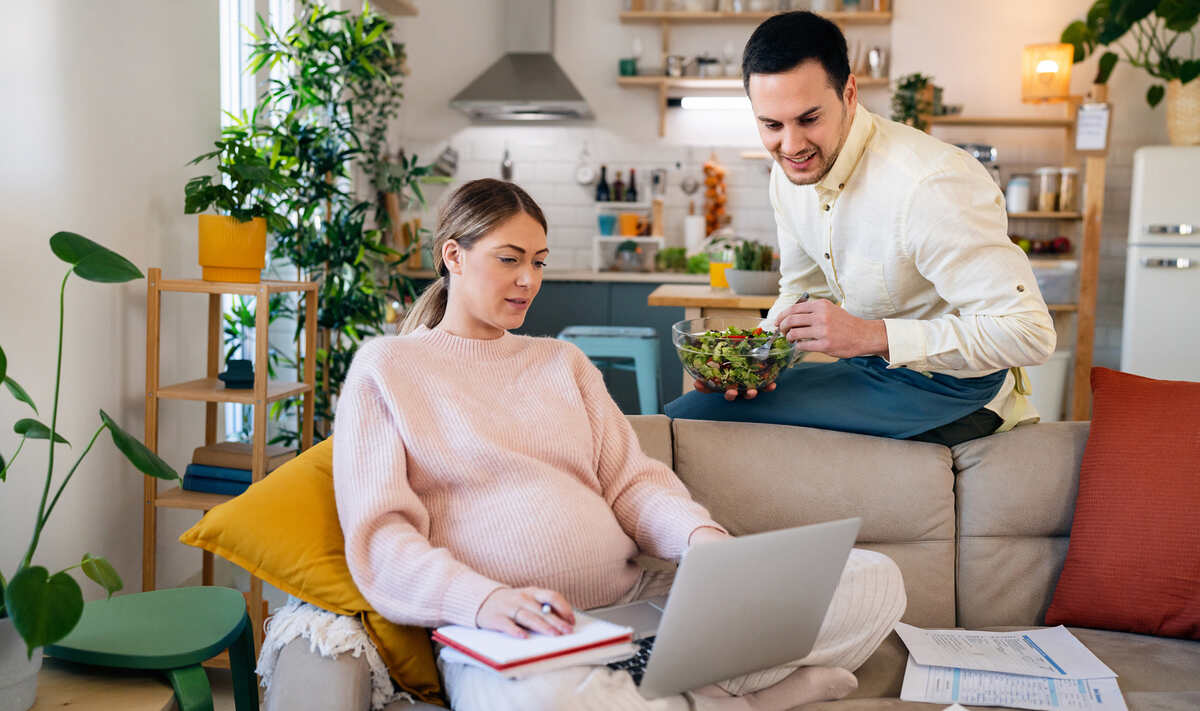terhes anyuka laptoppal a kanapén és a férje, babaváró hitel és csok igénylése közben