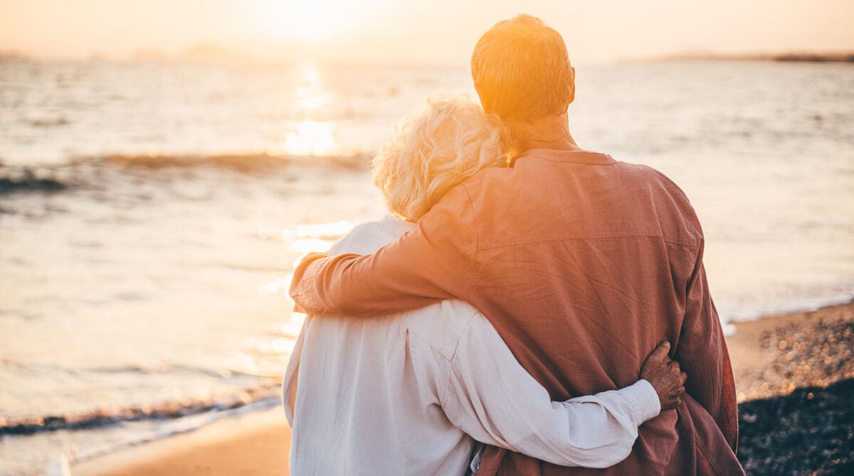 nyugdíjas házaspár a tengerparton, nyaralás közben, naplementében, nyugdíj megtakarítással a bankszámlájukon