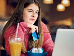 bankszámlanyitás gyerekeknek: a 18 év alatti lány a diák bankkártyájával ül a kávézóban, narancslével, laptoppal
