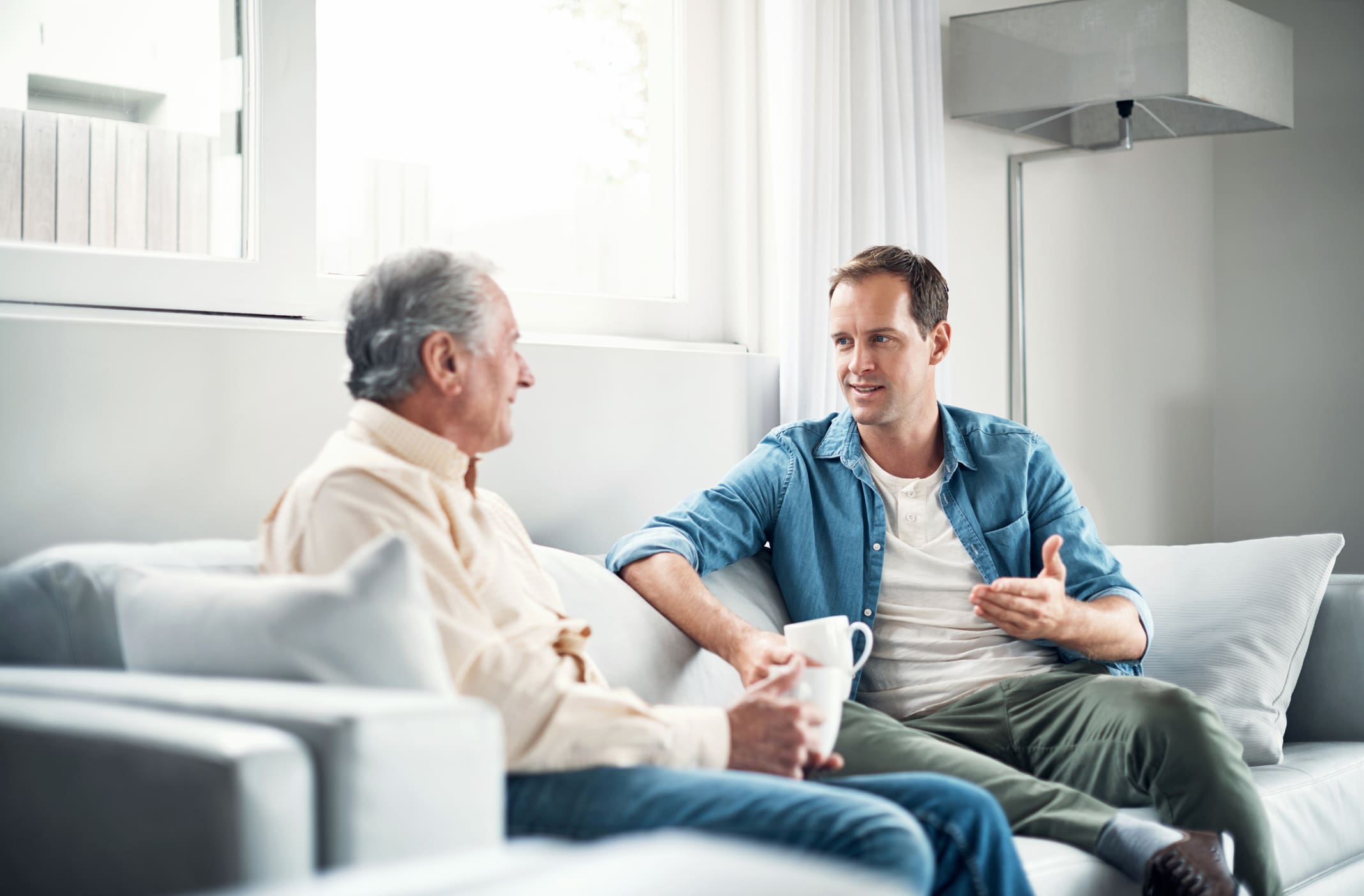 Egy férfi beszélget az apjával egy kanapén ülve egy szobában.